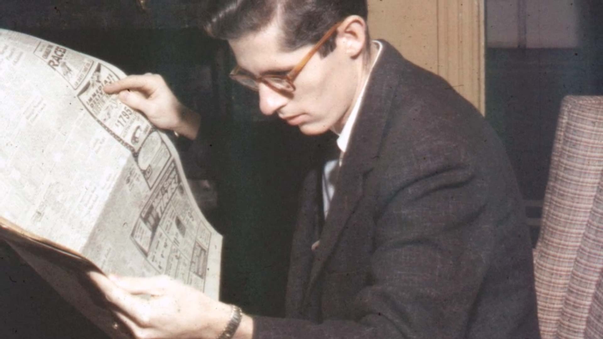 Man in suit reading newspaper in chair